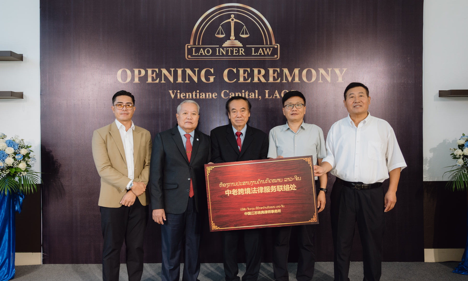 Five men standing at the LAO INTER LAW opening ceremony holding the red Laos-China Cross-Border Legal Services Liaison Office plaque.